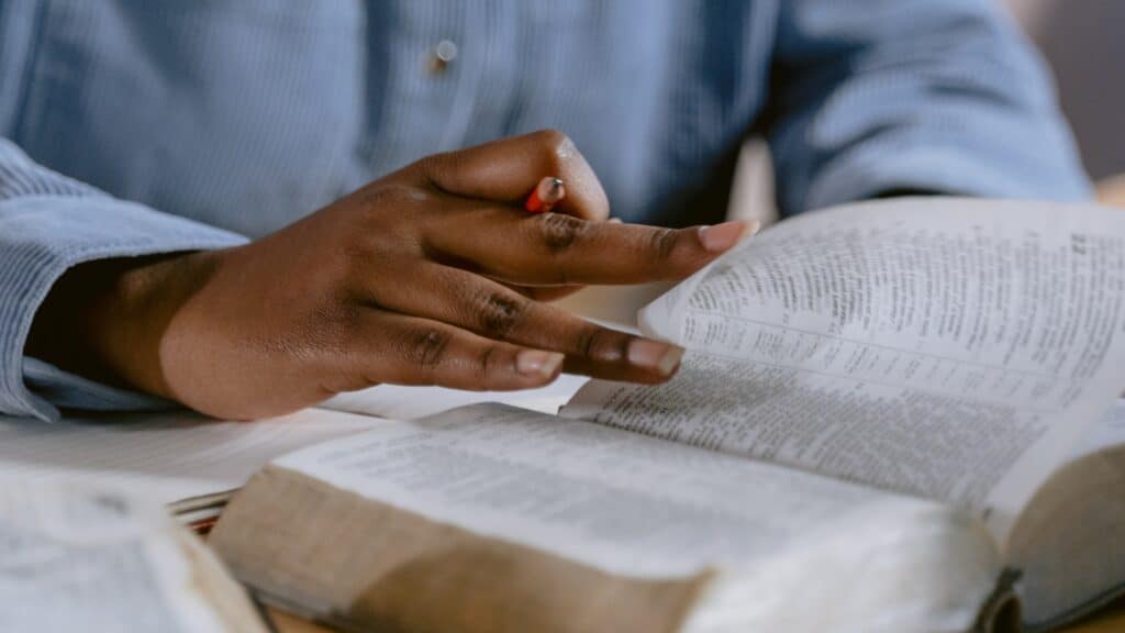 A person's hands paging through a Bible seated at a table.