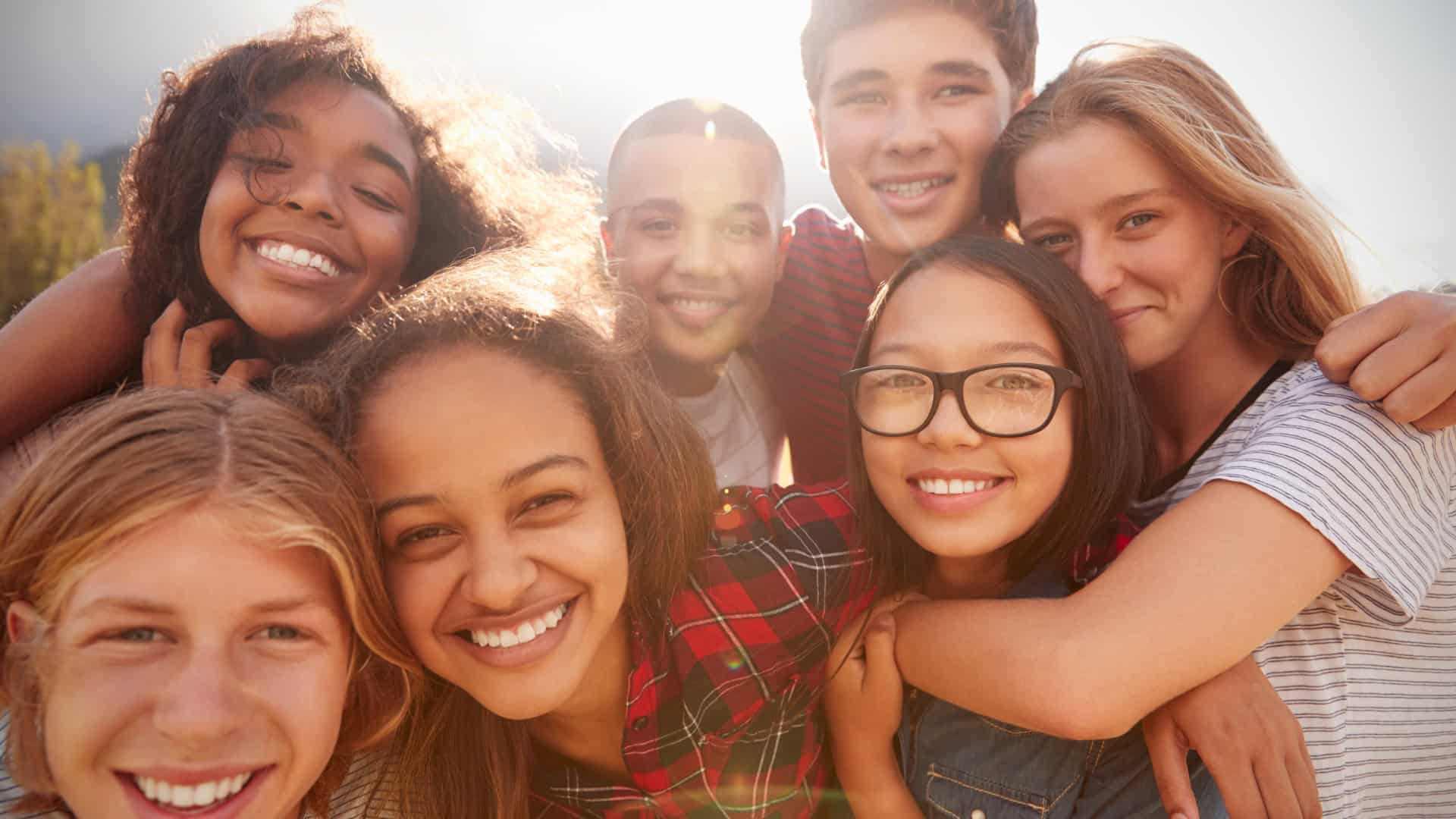 a smiling group of young people with sunlight glowing behind them