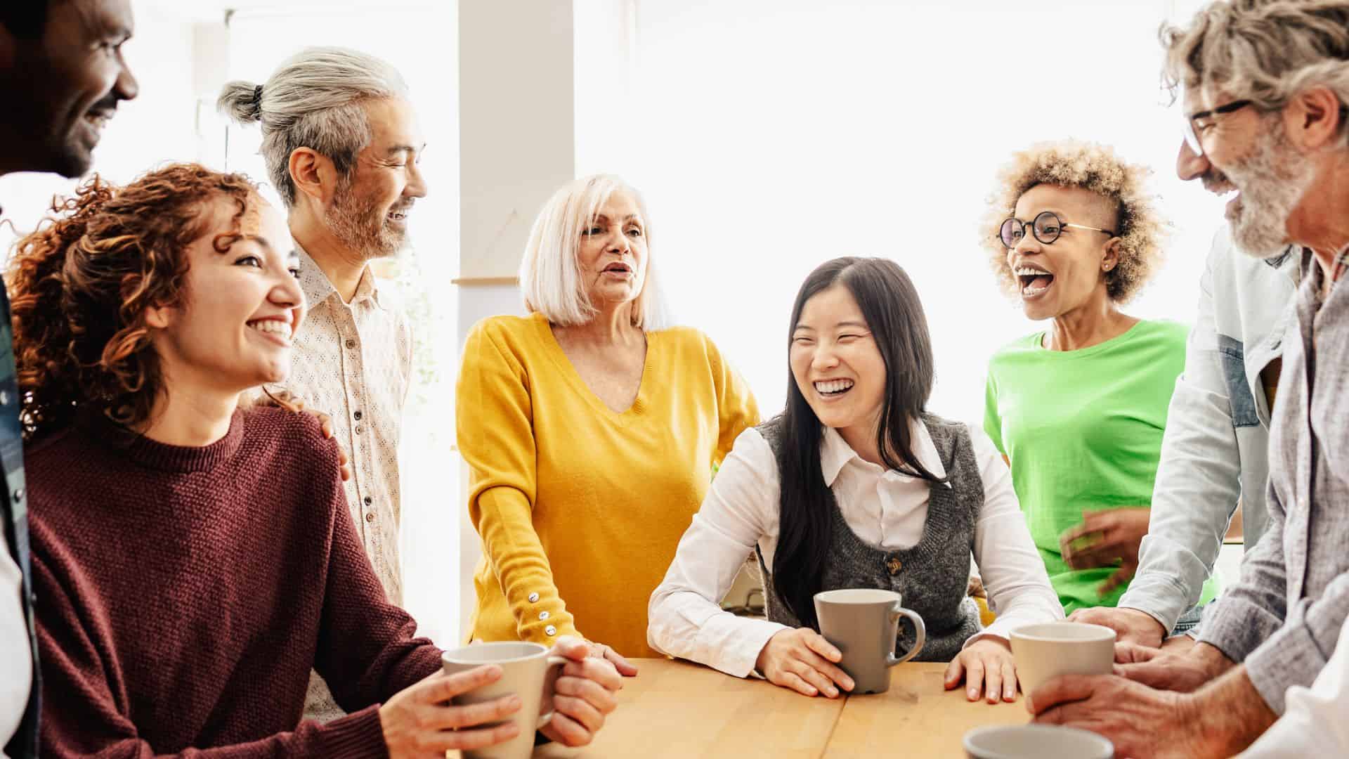 a group of smiling people standing around a table