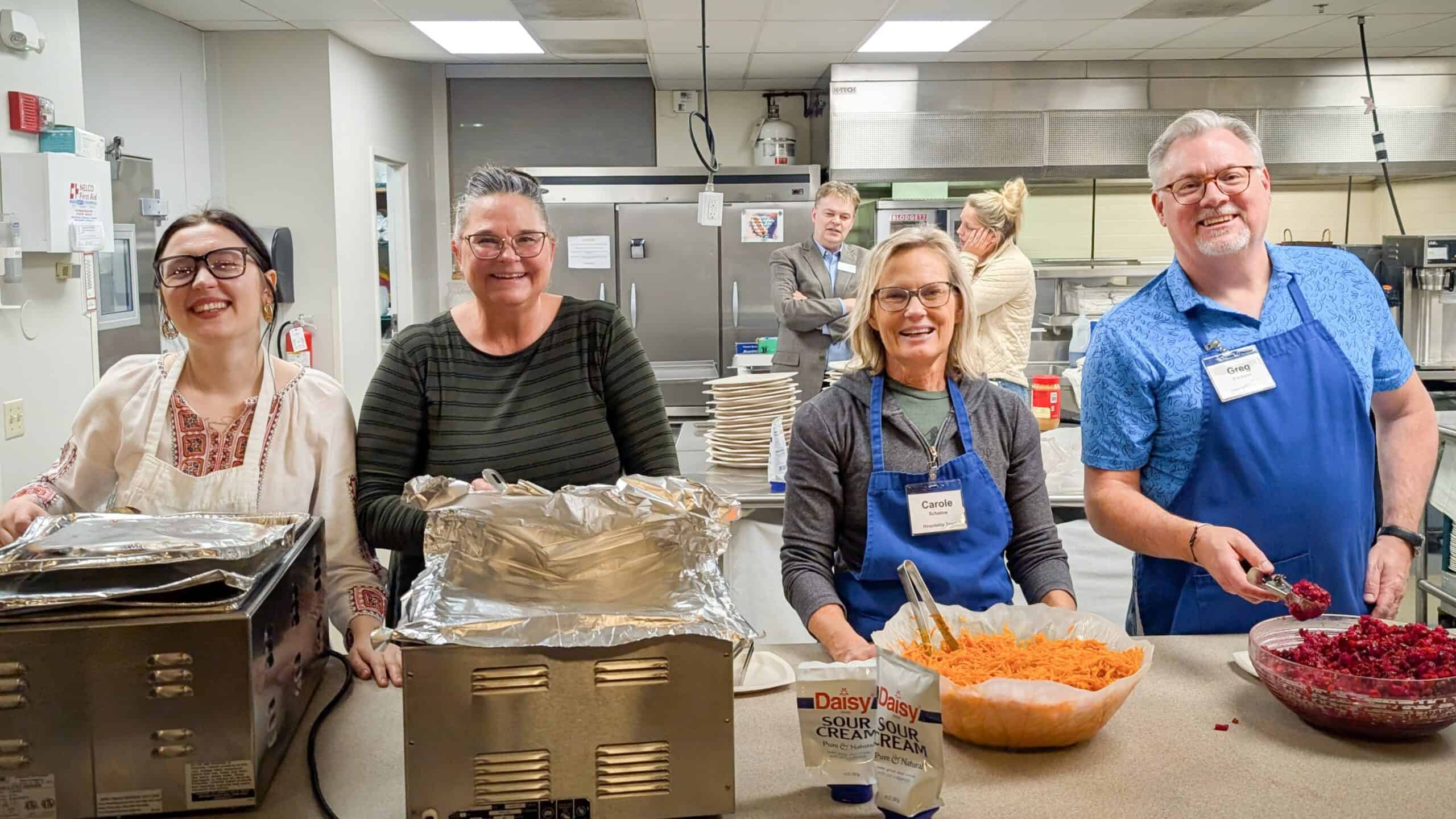 three happy women and a happy gentleman serving food from a kitchen window/countertop